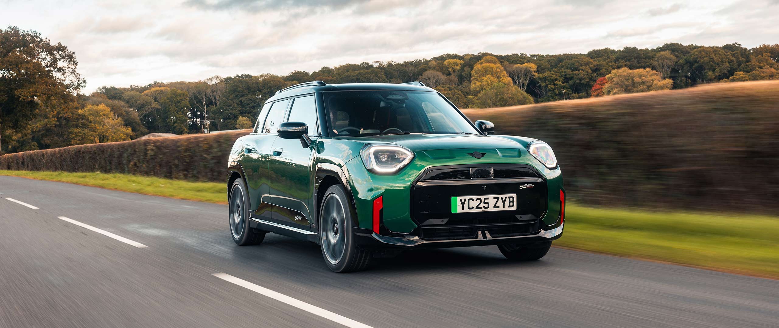 Front view of parking all-electric MINI Aceman in British Racing Green in car park with pink wall in the background